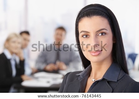 Portrait of attractive smiling businesswoman, team in background.?