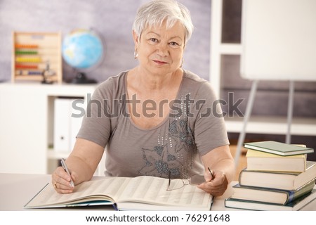 Portrait of senior teacher working at desk in classroom, looking at camera.?