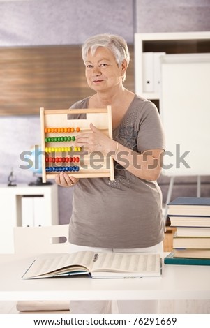 Senior teacher standing at desk, holding abacus, teaching math in elementary school.?