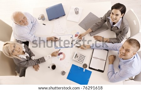 Happy businessteam working together, smiling, pointing at document, overhead view.?