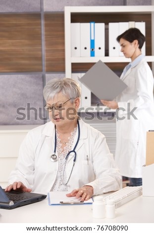 Senior doctor with young specialist working together in office, using computer and folder.?