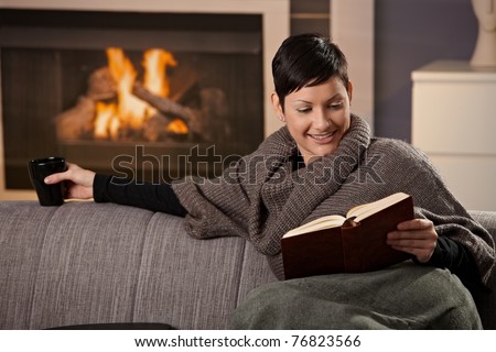 Woman sitting on sofa at home on a cold winter day, reading book.?