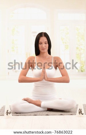 Young woman wearing white doing yoga exercise with closed eyes.?