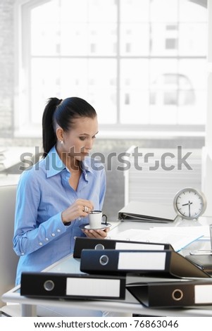 Busy businesswoman having coffee at desk, while looking at documents.?