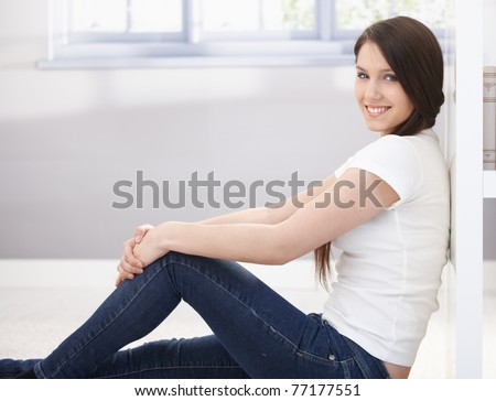 Happy college girl sitting on floor, smiling, looking at camera.?