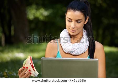 stock-photo-young-woman-in-park-at-lunchtime-using-laptop-eating-club-sandwich-77658586.jpg