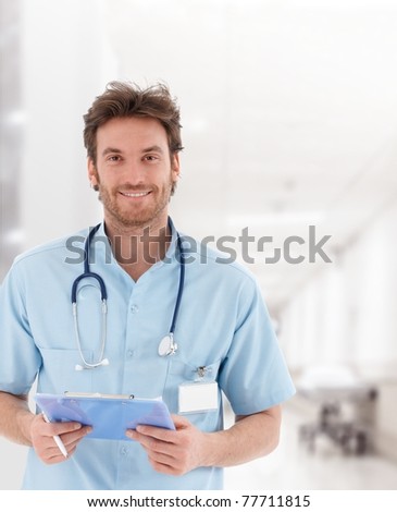 Portrait of handsome young doctor on hospital corridor looking at camera smiling Portrait of handsome young doctor on hospital corridor looking at camera smiling