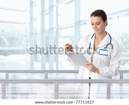 Female doctor using tablet computer in hospital lobby, smiling.?