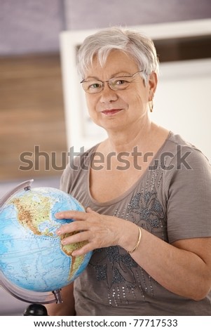Senior teacher standing at desk, pointing at globe, teaching geography in elementary school.?