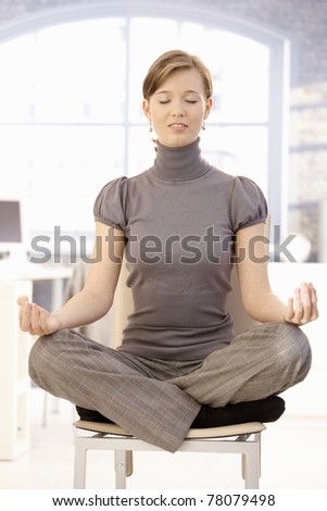 Attractive young businesswoman meditation in office, sitting at lotus position with closed eyes.?