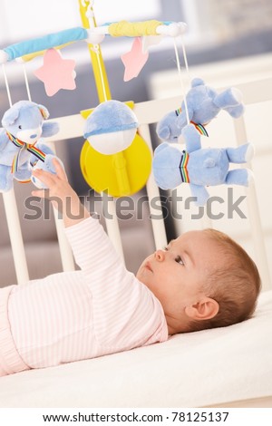 Baby girl playing in bed with mobile toy bear.?