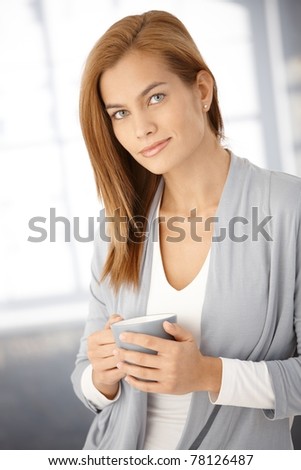 Portrait of attractive young woman holding tea mug, looking at camera, smiling.?