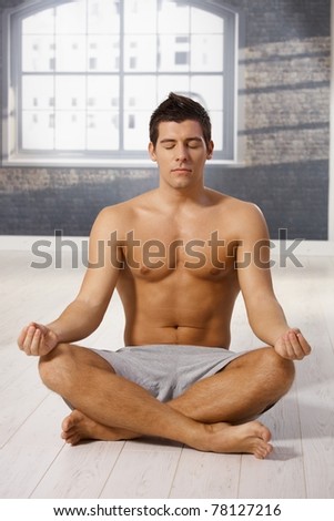 Athletic guy meditating in yoga position with eyes closed, sitting on floor.?
