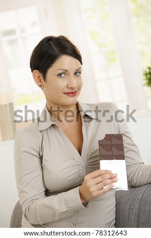 Guilty woman holding chocolate, looking at camera, eyebrows raised.?