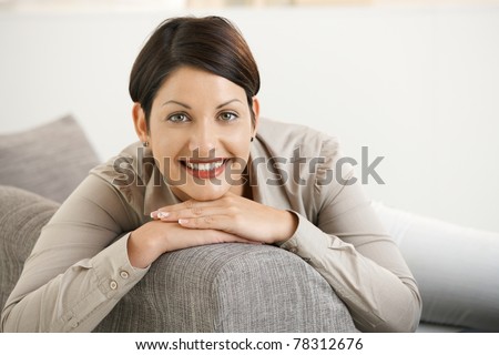Portrait of happy young woman sitting on sofa at home, leaning on back, smiling.?