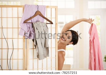 Happy young woman dressing up, looking out behind dressing panel, showing up pink shirt.