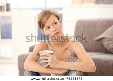 Casual young woman sitting on floor at home, holding tea in hand.?