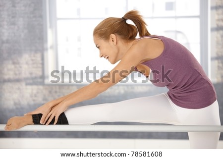 Happy ballerina stretching at bar, laughing at ballet class in exercise room.?