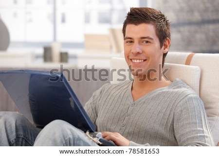 Portrait of cheerful young man using laptop computer at home, smiling at camera.?