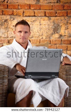 Portrait of handsome man in bathrobe sitting in armchair with laptop computer.?