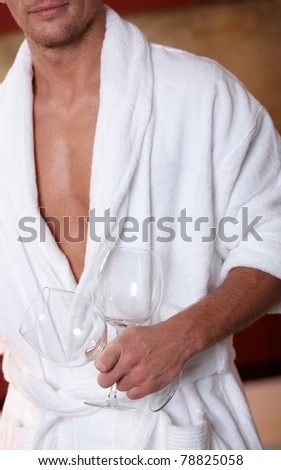 Sporty man in bathrobe holding wine glasses.?