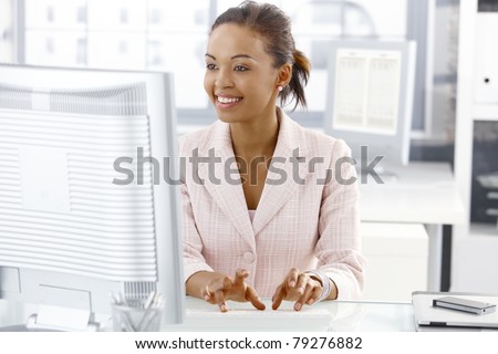 Happy office worker girl sitting at desk, working on computer, looking at screen.?