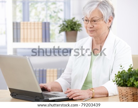Old lady sitting at desk at home, using laptop.?