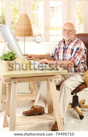Portrait of elderly man sitting at desk using desktop computer, smiling at camera.?