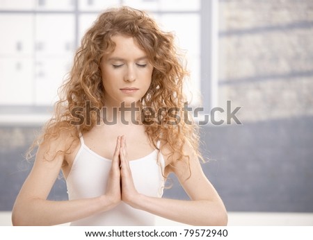 Attractive young female doing yoga exercise, meditating in prayer pose, eyes closed, sitting on floor front of window.?