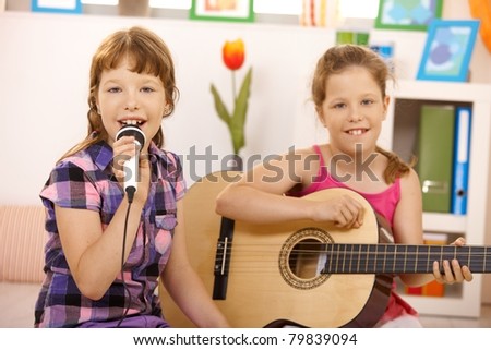 Portrait of young girls performing music, singing and playing guitar, smiling at camera.?