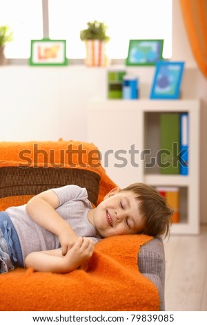 Little boy having nap, smiling in his sleep on couch in living room.?