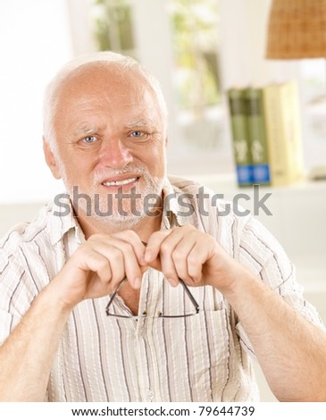 Portrait of white hair senior man holding glasses, smiling at camera.?