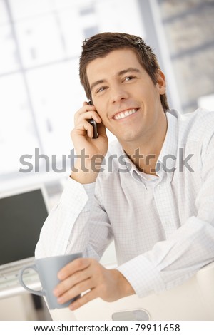 Happy businessman on mobile phone call laughing, holding coffee mug.?