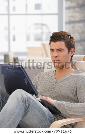 Handsome man concentrating on laptop computer screen, looking troubled, sitting in living room.?