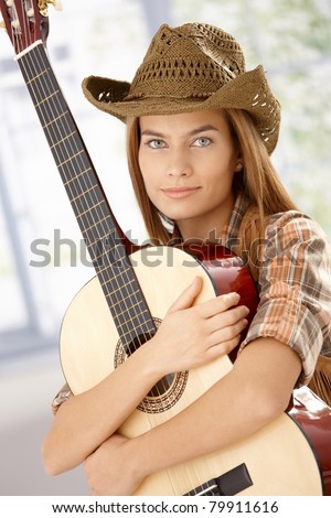 Attractive guitar player girl hugging her guitar, smiling, wearing western hat.?