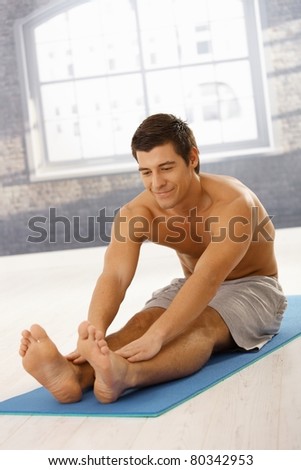 Happy sporty guy stretching in gym before training, smiling.?