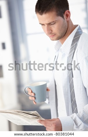 Young man reading newspaper in the morning, drinking tea.?
