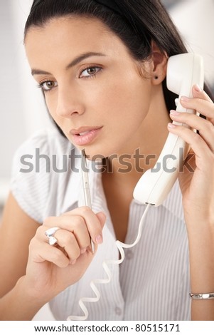 Attractive woman concentrating on landline phone call, thinking, holding pen.?