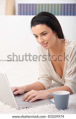 Woman using laptop computer at home, smiling at screen, lying in living room.?