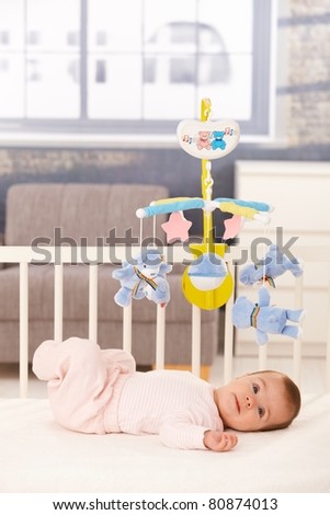 Little cute baby girl lying in crib with toy mobile.?