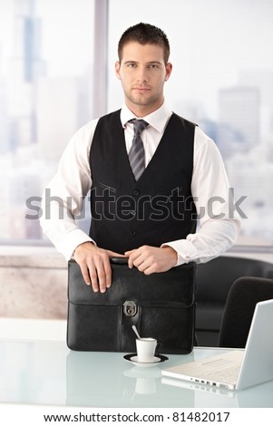 Young businessman standing at desk in bright office.?