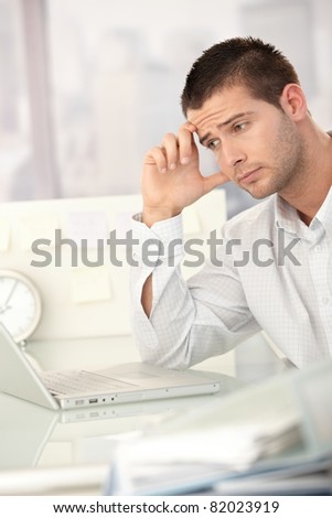 Tired businessman working on laptop in bright office.?