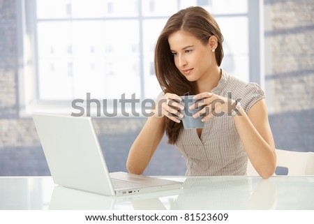 Beautiful smiling businesswoman at work looking at laptop computer screen, having tea.?