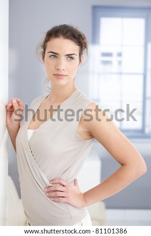 Attractive young woman standing front of window, looking away.?
