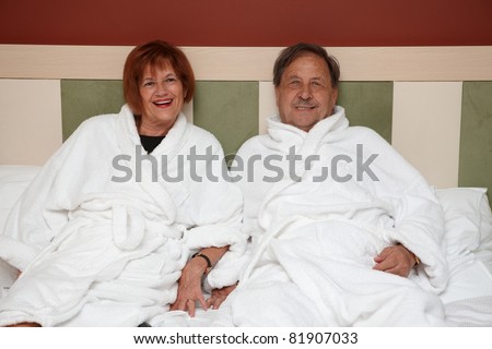 Happy mature couple laying on bed at wellness hotel, smiling, looking at camera.?