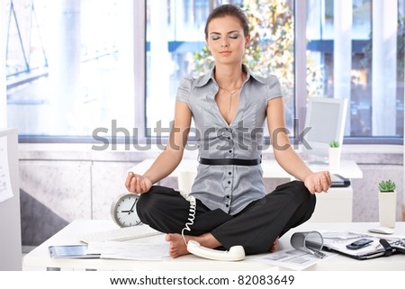 Young office worker meditating on top of desk in bright office.?