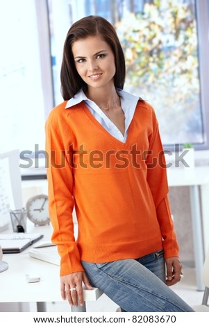 Pretty office worker smiling in orange pullover in bright office.?