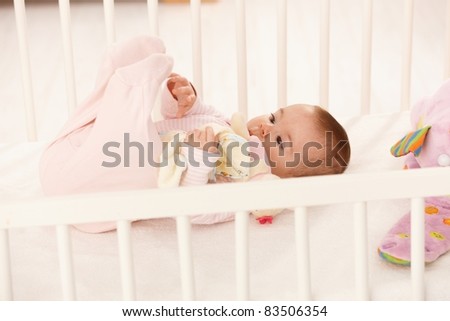 Cute baby playing with feet in baby crib, holding toy.?