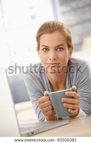 Portrait of happy pretty woman lying on couch with coffee mug and laptop computer, smiling at camera.?