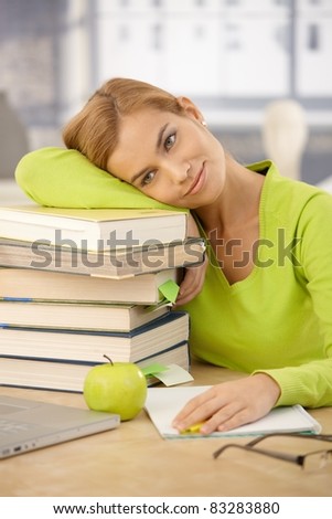 Portrait of smiling university girl relaxing on pile of books at desk at home.?